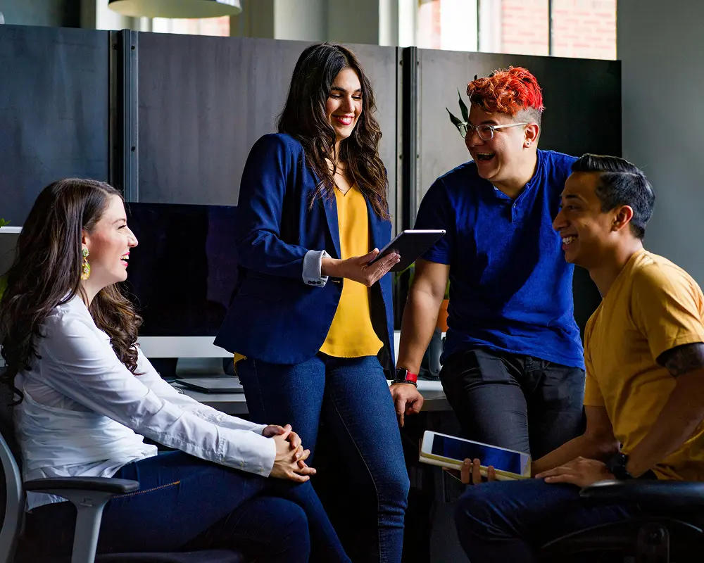 cuatro jóvenes, sentados y de pie alrededor de una mesa de trabajo